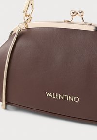 Brązowa skórzana torba na ramię z złotym zapięciem, posiadająca teksturowaną powierzchnię i metalowy akcent na suwaku. Nazwa marki "VALENTINO" w złotym napisie.