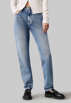 Jean en denim bleu clair avec une coupe décontractée et une finition délavée ; il possède cinq poches, des passants de ceinture et une coupe droite. Associé à des mocassins noirs.