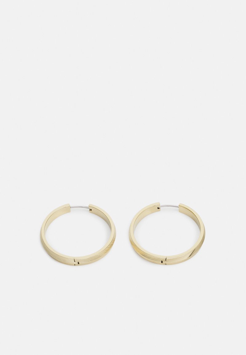 Boucles d'oreilles créoles en ton doré avec une finition lisse et texturée. Forme circulaire au design minimaliste. Équipées d'une fermeture à charnière pour un port sécurisé.