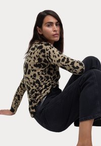 Maglione a maniche lunghe con stampa leopardata in tonalità beige e nero, abbinato a pantaloni in denim scuro, con polsini a coste e vestibilità comoda.