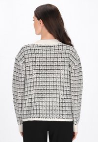 Kézzel kötött krémszínű pulóver fekete rácsmintával, környakú kivágással és bordázott mandzsettákkal. Texturált anyagú, laza szabású darab.