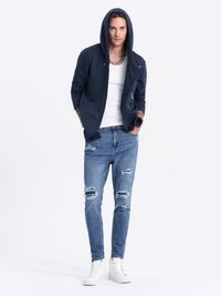 Marinehætte sweatshirt, hvid tank top, slidte lyseblå jeans og hvide høje sneakers. Har lynlåse og flere revner i jeansene.