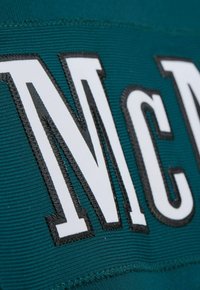 Nahaufnahme des weißen NY Giants-Logos, das mit schwarzem Faden auf strukturiertem dunkelgrünem Stoff gestickt ist.