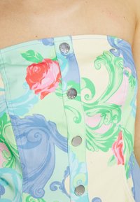 Haut sans bretelles à motif floral mêlant des tons pastel vert, rose et bleu, avec des boutons en métal argenté sur le devant. Tissu en coton.