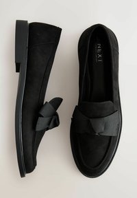 Schwarze Wildleder-Slipper mit flacher Gummisohle, versehen mit einer strukturierten Schleife vorne und einem glatten Futter.