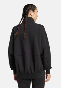 Black oversized sweatshirt with a high collar, dropped shoulders, and gathered hem. Smooth fabric with a relaxed fit and long sleeves.