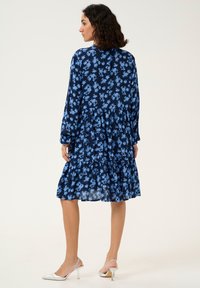 Robe florale bleu marine avec une jupe à volants, des manches longues et une coupe ample. Caractéristiques de fleurs bleu clair et d'un tissu doux et léger.