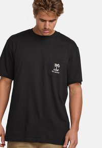 Camiseta de algodón negra con cuello redondo, bolsillo en el pecho con un logo de palmera blanca y mangas cortas. Textura suave, corte relajado.