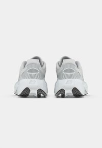 Une paire de baskets de sport grises et blanches vue de l'arrière, montrant des semelles de talon striées et le logo de la marque sur les semelles intermédiaires.