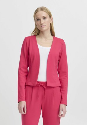 Fialový přiléhavý blazer z měkké látky, s hlubokým výstřihem a dlouhými rukávy, v kombinaci s bílým tričkem a ladícími růžovými kalhotami. Minimalistický design.