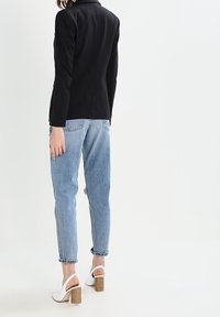 Blazer noir cintré associé à un jean taille haute bleu clair, des mules blanches à talons carrés et une coiffure simple et lisse.