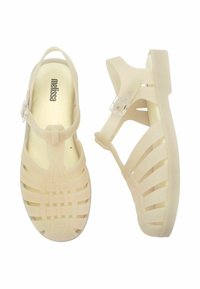 Przezroczyste beżowe sandały z żelatyny z plecionym wzorem paska, okrągłym noskiem i regulowanym przezroczystym zapięciem dla pewnego dopasowania.