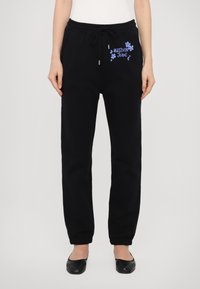 Musta collegehousut, joissa on joustava vyötärö, narukiinnitys ja sininen kukkakuosiset Moschino Jeans -logot edessä.