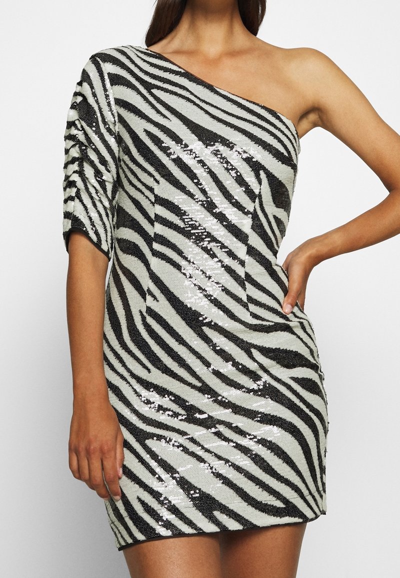 Robe asymétrique à une épaule avec des rayures zèbre noires et blanches, en tissu pailleté, présentant une silhouette ajustée et un design à manches courtes.