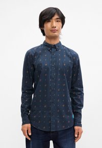 Ναυτική πουκάμισο μ ε λουλουδάτο μοτίβο, μακριά μανίκια και slim fit. Περιλαμβάνει γιακά που κλείνει με κουμπί και λεπτομέρεια με ετικέτα στο πλάι.