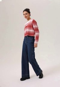 Rood-wit gestreepte cardigan, ribbeltextuur, knoopsluiting, gecombineerd met hooggezette donkerblauwe wijde jeans en zwarte schoenen.