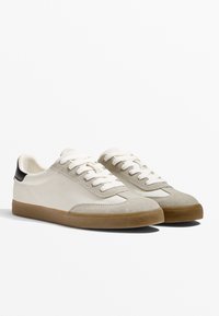 Sneaker mit einem glatten, cremefarbenen Lederobermaterial, einer grauen Wildlederspitze und einer strukturierten, beige-gummierten Sohle. Mit weißen Schnürsenkeln und einem schwarzen Absatzakzent.