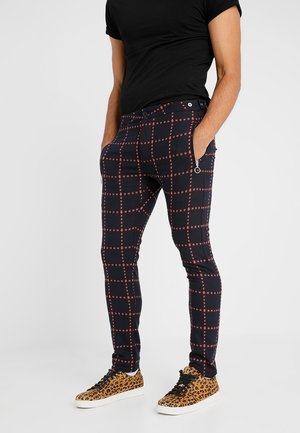 Pantalons slim-fit bleu marine avec un motif à carreaux rouges. Comprend des poches latérales et un accent zippé. Associés à des chaussures à imprimé léopard.