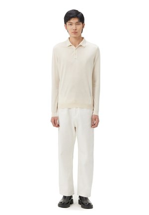 Helle beige langärmlige Polohemd aus weichem Stoff, mit einer Knopfleiste mit drei Knöpfen, kombiniert mit locker sitzenden weißen Hosen und schwarzen Stiefeln.