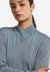 Niebieski sweter dzianinowy z krzyżowym dekoltem. Wykonany z miękkiego materiału, ma gładką fakturę i długie rękawy.