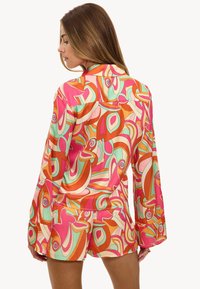 Conjunto de pijama de seda con estampado colorido que presenta tonos vibrantes de rosa, naranja y turquesa. Incluye una camisa de manga larga y pantalones cortos de corte holgado.