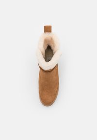Bottine en suede marron avec une doublure en fourrure crème, bout rond et une petite languette à l'arrière pour un enfilage facile.