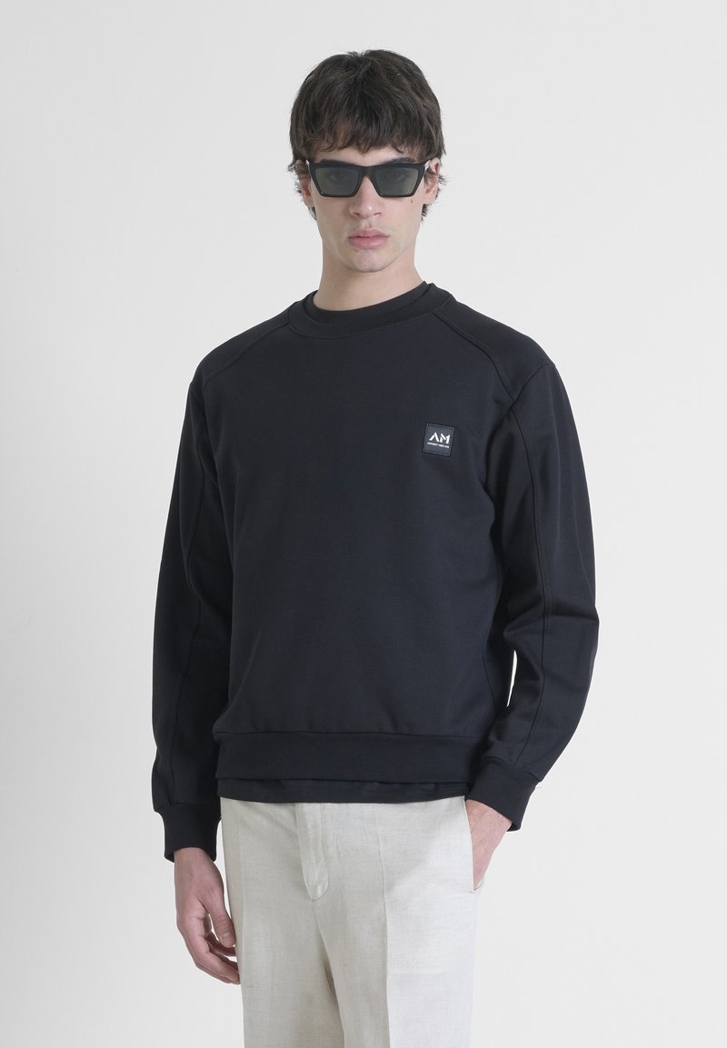 Crna sweatshirt s okruglim izrezom, raglan rukavima i malim logotipom na liješoj strani prsnog koša. Glatka tekstura i opušten fit.