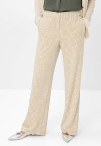 Pantaloni beige a gamba larga realizzati in tessuto testurizzato con un delicato motivo floreale. Presentano una vita elastica e tasche laterali.