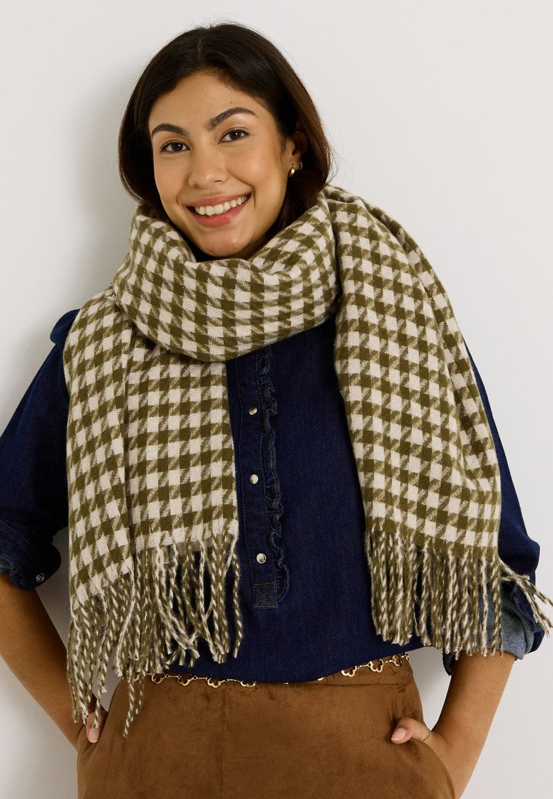 Bufanda de tejido con un patrón a cuadros en verde y beige, con bordes fringidos, mostrada envuelta alrededor del cuello del modelo.