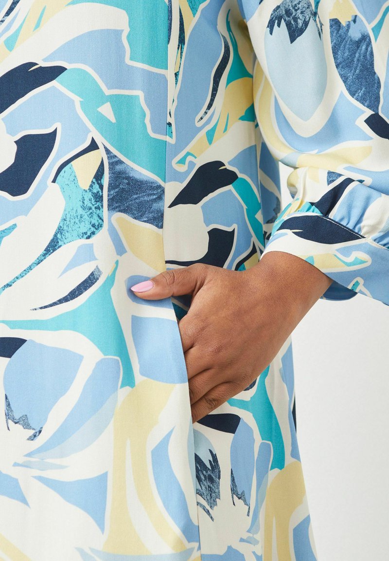 Langärmliges Kleid aus leichtem Stoff mit einem blauen, weißen und gelben Blumenmuster, seitlicher Tasche und gerafftem Ärmelabschluss.