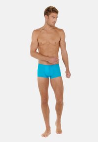 Pantaloni boxer turchesi realizzati in tessuto elastico, con un design aderente e una texture liscia. Indossati da un modello maschile su uno sfondo bianco.