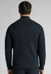Pull en tricot bleu foncé avec un motif de cable texturé, des poignets côtelés et un col rond. La coupe est ample, adaptée à un style décontracté.