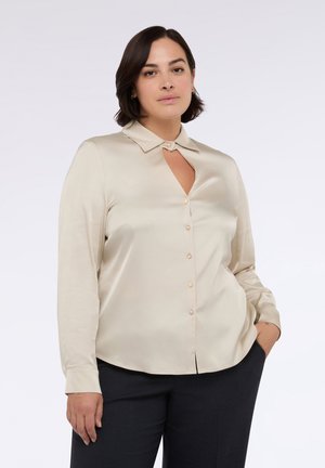 Camicia in satin di colore crema, a maniche lunghe, con colletto, un'apertura a forma di chiave sul petto e bottoni perlacei lungo il davanti. Tessuto liscio e design aderente.