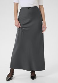 falda larga y ajustada de satén gris con una textura suave, cinturilla elástica y pequeño detalle de lazo en la parte delantera, combinada con tacones negros.