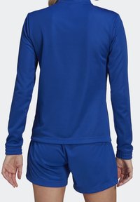 Conjunto atlético azul que incluye una camiseta de manga larga y un pantalón corto. La tela parece suave y elástica, con un ajuste confortable y detalles sutiles.