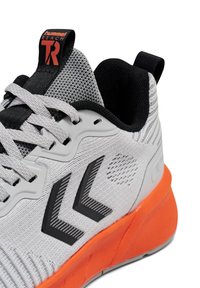 Grijze sneaker met zwarte accenten en oranje zool. Voorzien van een bovenwerk van mesh, opvallende logo's en gestructureerde patronen aan de zijkant en hiel.