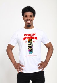 Bílý bavlněný tričko s grafickým designem skateboardu se skull motivem a barevnými květinovými prvky, doplněné červeným textem.