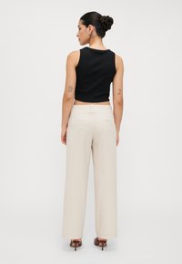 Top cropped nero abbinato a pantaloni beige a gamba larga a vita alta. Scarpe con tacco marroni e gioielli minimalisti completano il look.