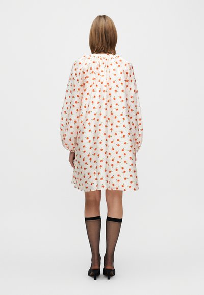 Hosszú ujjú, térdig érő ruha krémszínű anyagból, apró narancssárga virágmintákkal. Rugalmas nyakkivágás és gyűrt felsőrész. Fekete combfixszel viselve.