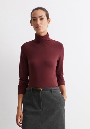 Burgundy turtleneck top with long sleeves, made of soft fabric. Paired with a gray skirt and a black belt with a gold buckle.
