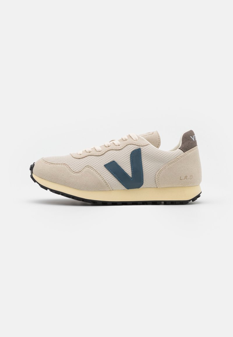 Basket beige et crème avec un grand logo V bleu foncé sur le côté, semelle noire et lacets blancs, présentée sur un fond blanc.