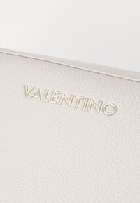 Borsa in pelle Valentino di un beige chiaro con una finitura texturizzata. Caratterizzata da un logo dorato impresso, che mette in risalto un design semplice e pulito.