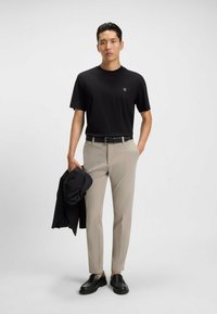 Czarna koszulka z krótkim rękawem z logo, beżowe slim-fit spodnie, czarny pasek oraz czarne buty typu slip-on; trzyma czarną kurtkę.