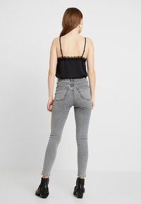 Camiseta sin mangas negra con encaje en los bordes y tirantes finos, combinada con jeans ajustados gris de cintura alta. La modelo lleva botas negras de tobillo.