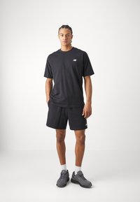 Black cotton t-shirt with short sleeves and a small logo, paired with matching black shorts. Footwear is gray athletic shoes.