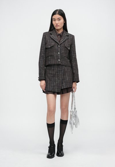 Pruun tweed-stiilis bleiser kahepoolses taskus, millele on sobitatud sama kangast seelik. Modell kannab musti põlvikuid ja massiivseid musti kingi, käes hõbedane kott.