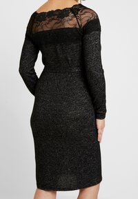 Abito lungo nero con maniche lunghe e silhouette aderente, caratterizzato da una schiena in pizzo trasparente e tessuto testurizzato. Lunghezza a metà polpaccio con scollatura tonda.