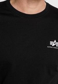 Czarny bawełniany t-shirt z okrągłym dekoltem i białym logo na lewej stronie klatki piersiowej. Materiał jest gładki z lekkim naciągiem.