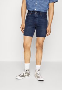 Jeansshorts i mörk tvätt med fransar i kanten. Kombineras med en blå randig kortärmad skjorta och högtoppsskor med zebramönster i svart och vitt.