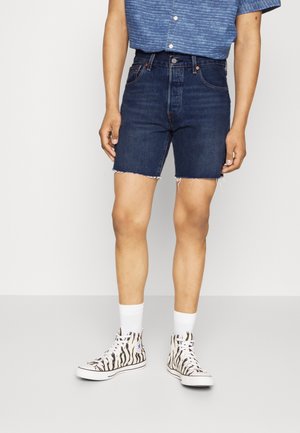 Jeansshorts i mörk tvätt med fransar i kanten. Kombineras med en blå randig kortärmad skjorta och högtoppsskor med zebramönster i svart och vitt.